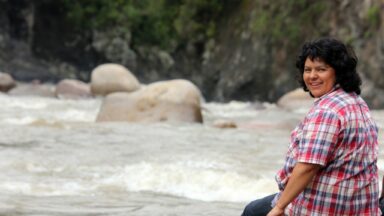 Berta Caceres sitting near a river, looking back over her shoulder and smiling