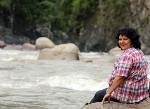 Berta Caceres sitting near a river, looking back over her shoulder and smiling