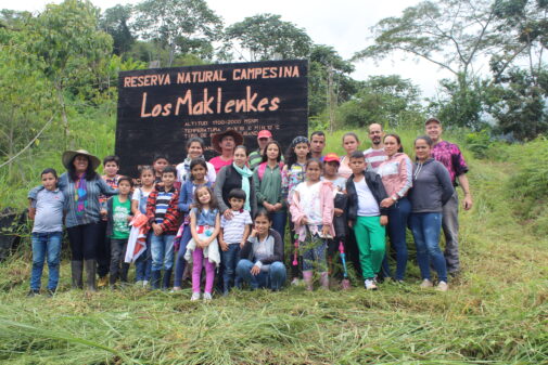 A group of people standing in a forest around a sign that says "los maklenkes" community nature reserve