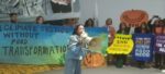 Asian woman speaking into megaphone in front of a protest action at cop29